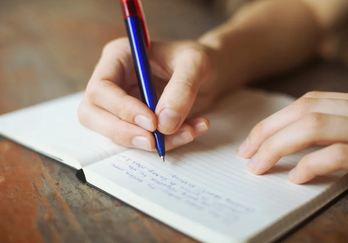 Hand writing in a notebook with a pen.